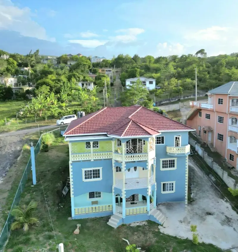 Aerial view of the three-storey house: pale blue walls, a red roof and balconies on the upper floors