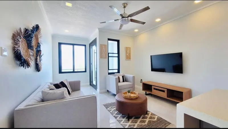 Living room with a grey sofa, round ottoman and windows to the balcony