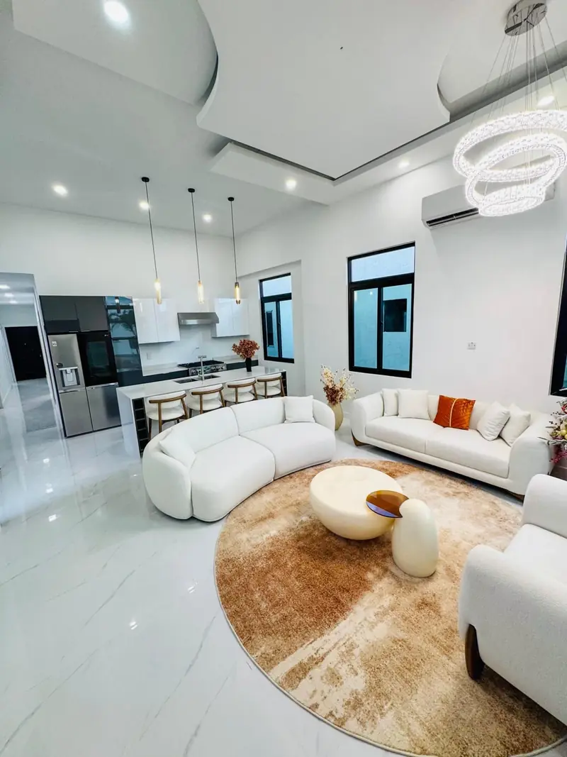 Open-plan living room with white sofas, a round rug and the kitchen behind